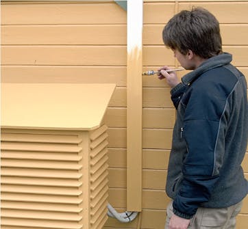 Kabelkanal til varmepumpeskjuler males Den hvide kabelkanal til varmepumpeskjuler males